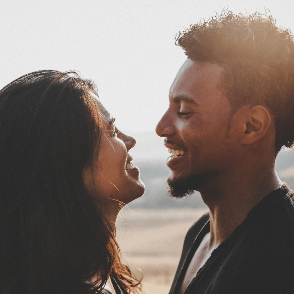 an image of a black man and an asian woman facing each other smiling