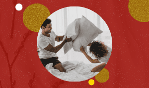 A couple having pollow fight above the bed in white sheets. Red background with circles that are in gold glitters, white, and yellow.