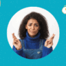 a feature sized image for the blog "Should I Text Him? How To Know What To Do" on a bright blue background with dotted texture. A black woman with a smirkng face wearing jumper jeans with a blue sweater inside while both hands on her shoulder level keeping fingers crossed. Yellow graphic circles surrounding her.