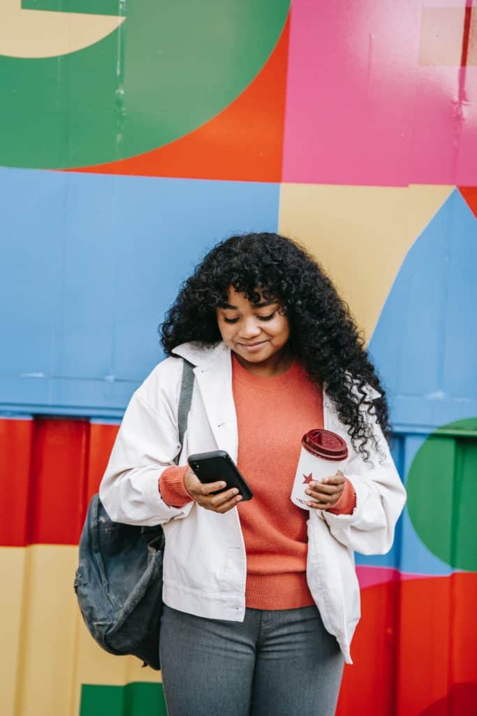 a smiling black woman using her smartphone near colorful wall