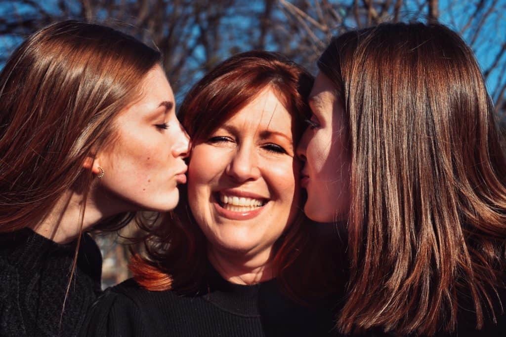 two woman kissing a woman's cheeks , one on the left and one on the right to show love