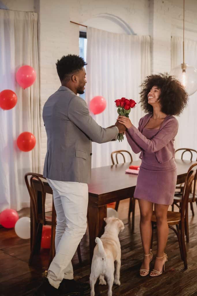 a black man handing over a boquet of roses to a black woman wearing an old rose dress