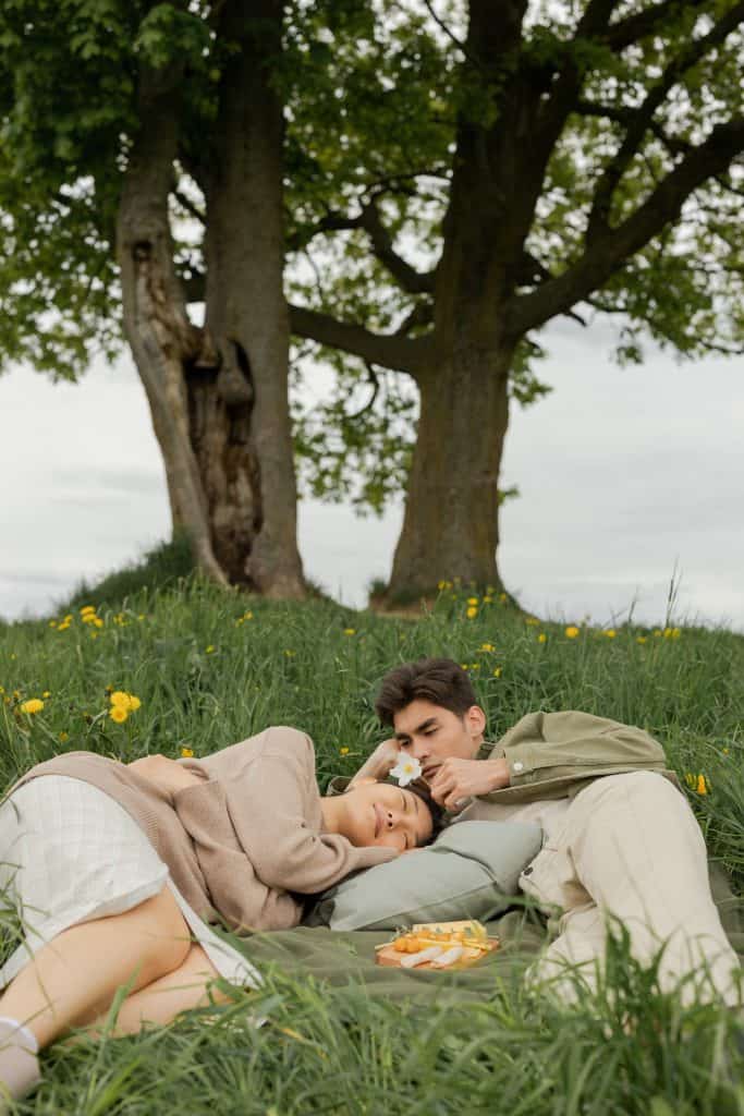 a couple dating and lying on grass under a big tree