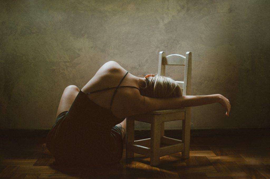 woman wearing a sexy black lingerie sitting on floor while leaning on a white chair