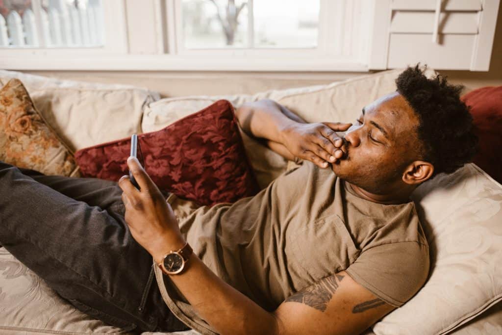 a black man lying on the coach with his phone on his left hand and right hand on his lips